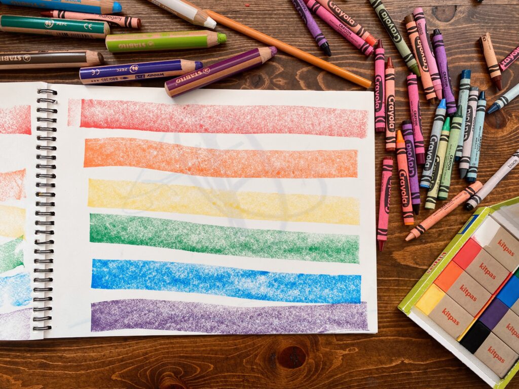 Sketchbook with hand drawn Pride flag surrounded by crayons