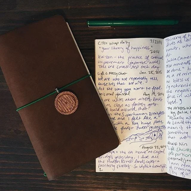 Traveler's notebook with wooden hobbit hole charm filled with small handwritten text and a green pen.