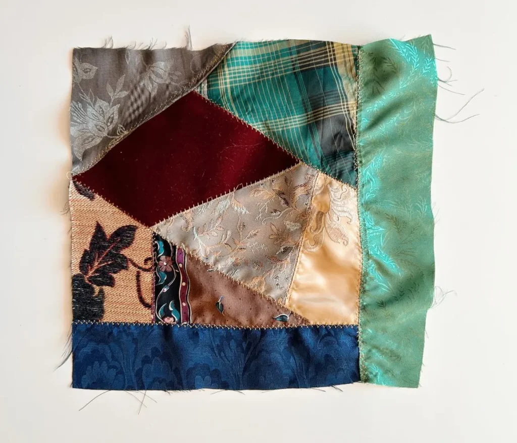 Crazy quilted square of textures like silk and velvet jewel tones sewn with golden thread and frayed edges