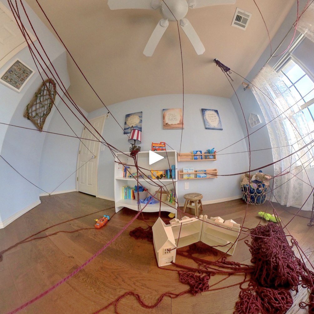 Still frame of 360 VR experience. A white play button floats over a nursery. Dark red yarn is strung around the room.