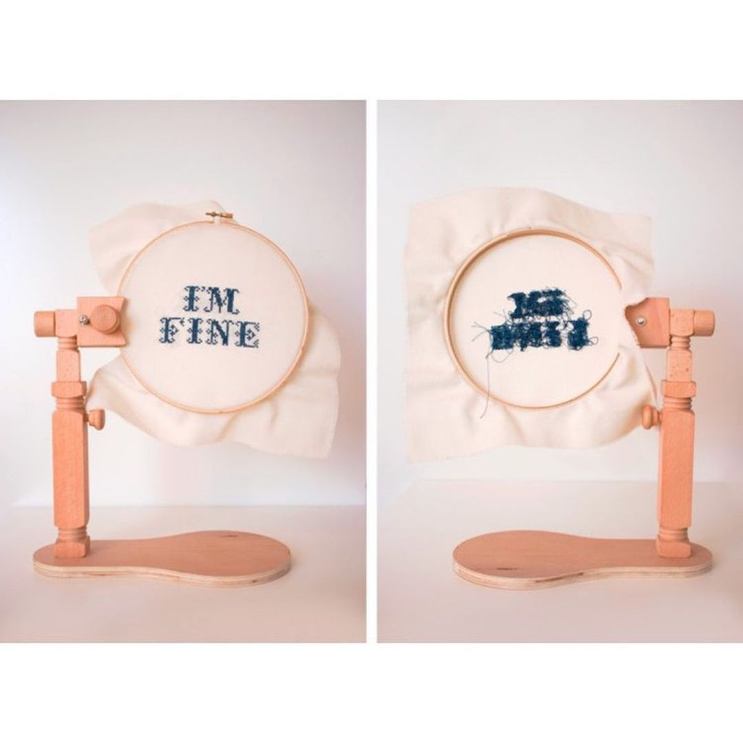 An embroidery frame holds a cross stitch that reads "I'm Fine". A second image shows the reverse which is a tangled mess of navy blue thread.