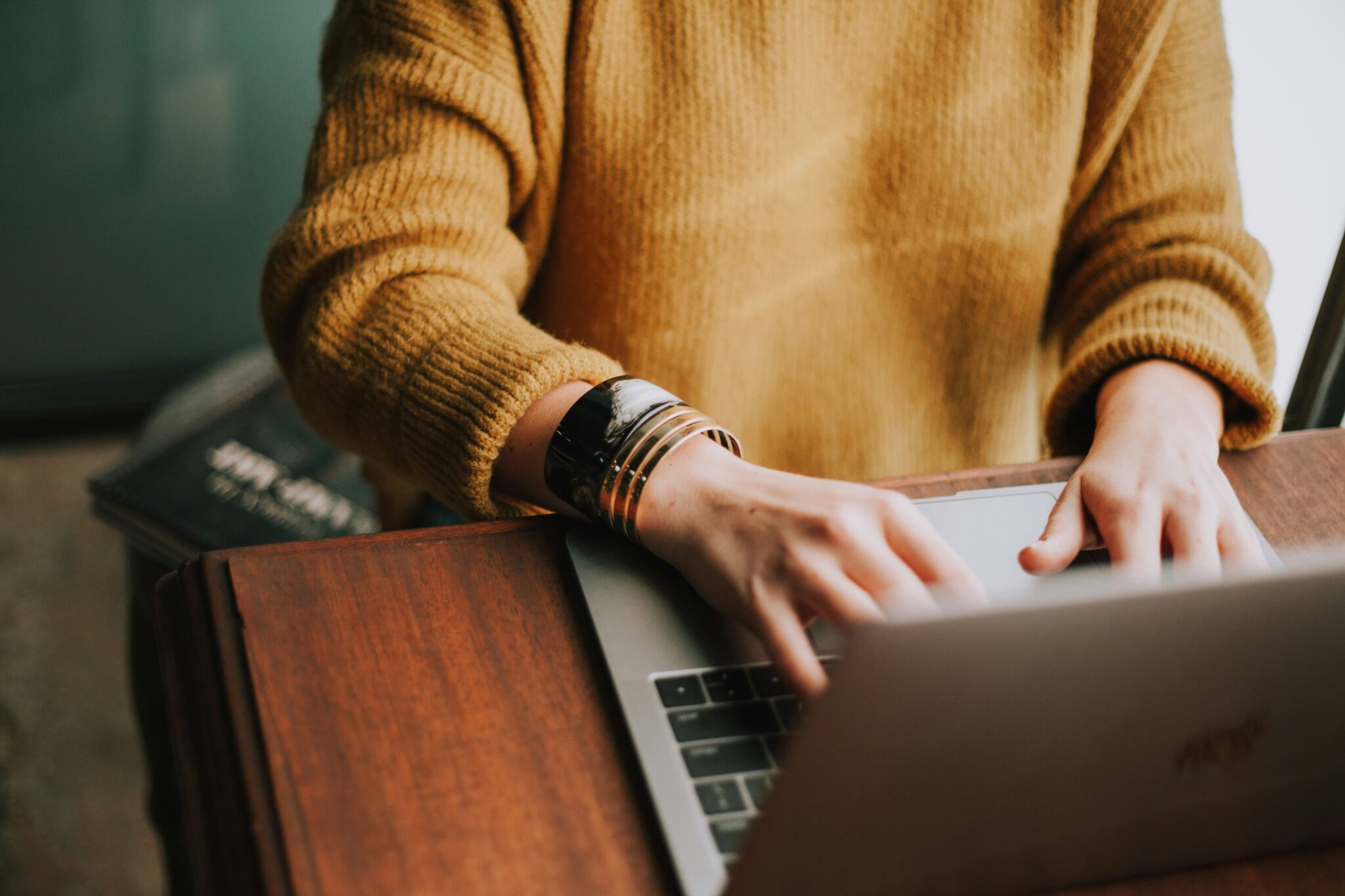 Person in a yellow sweater typing on a laptop