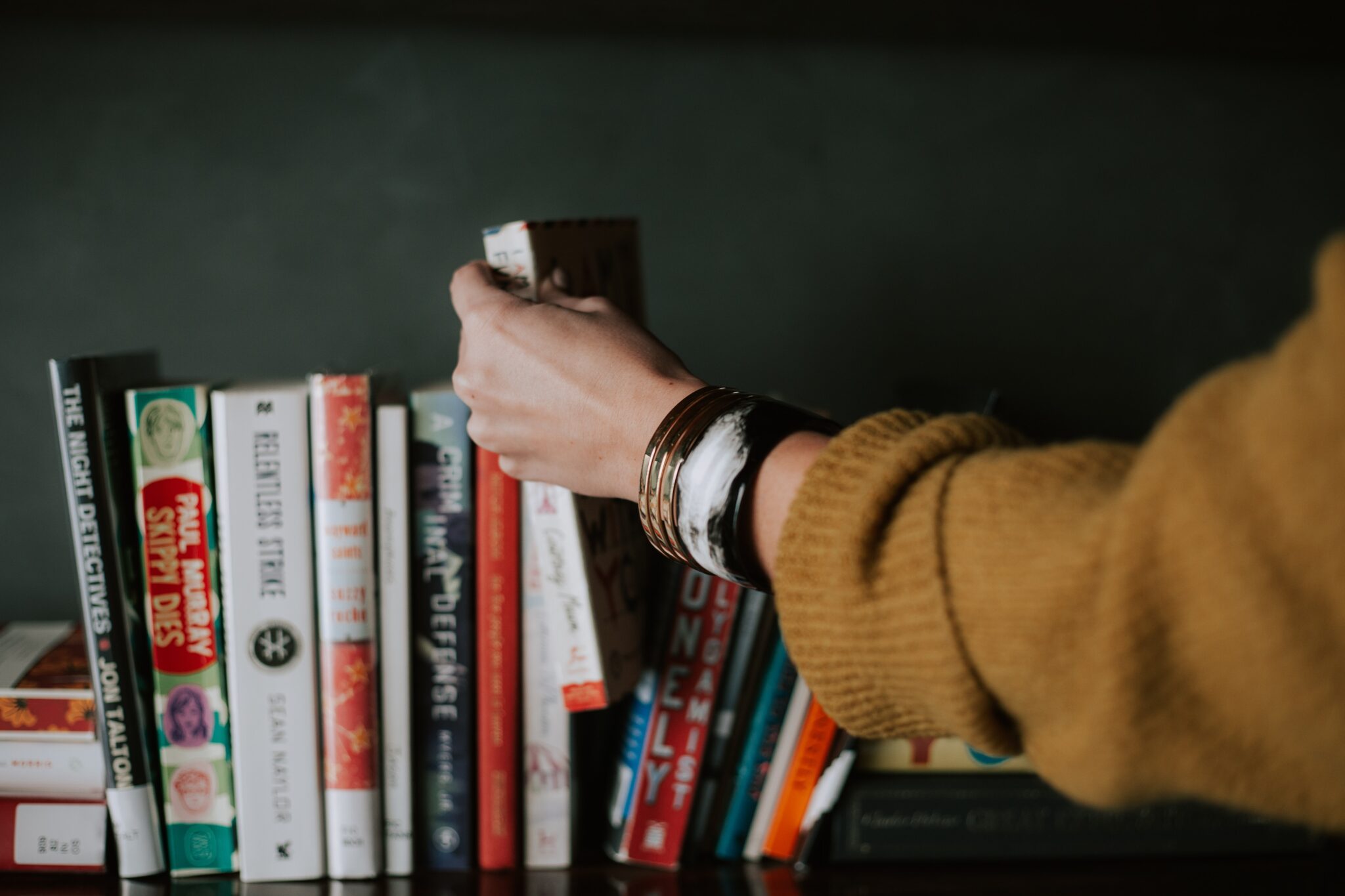 Arm in a yellow cardigan reaches to pull a book off a shelf