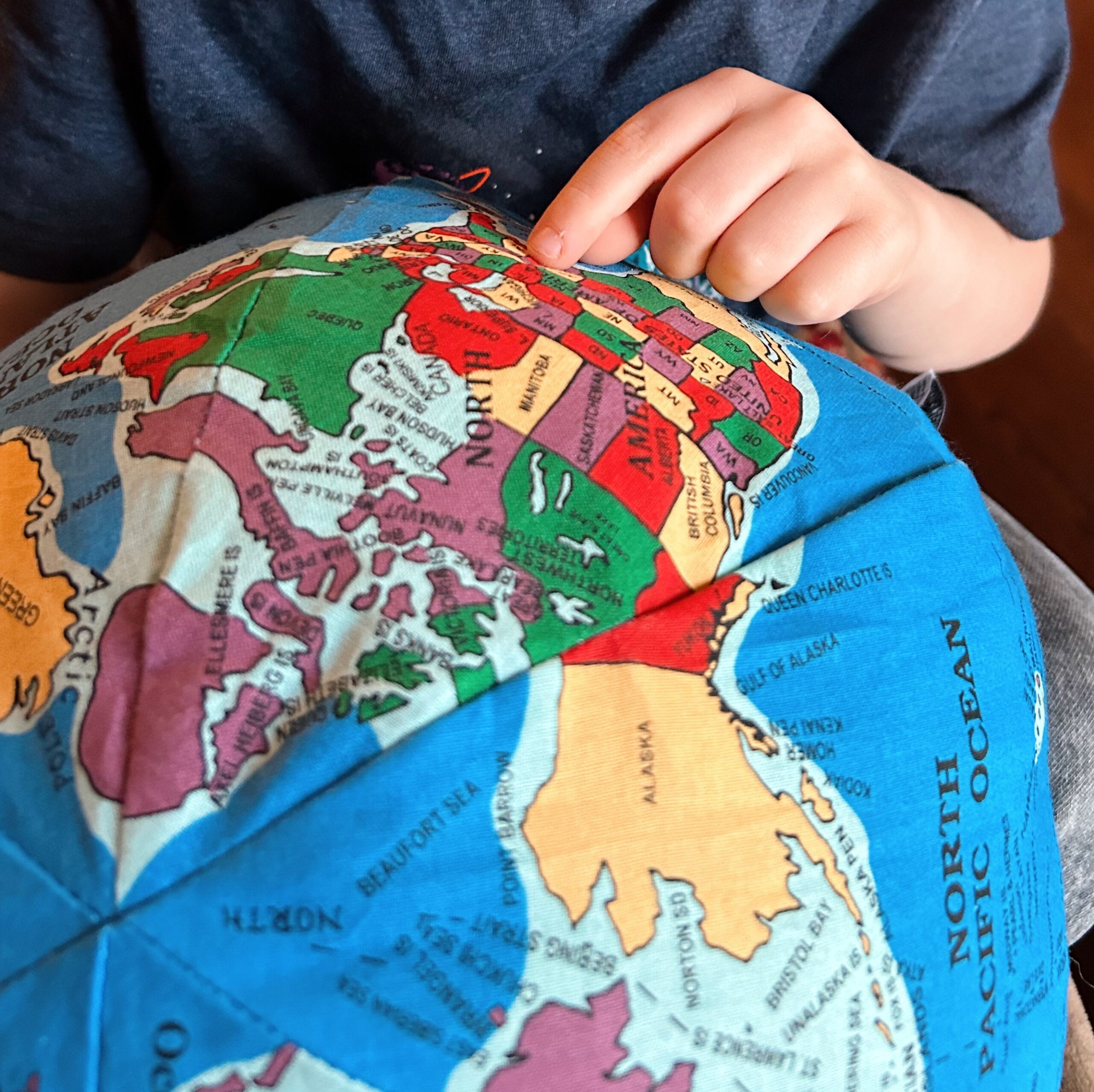 Pale hand points to a country on a soft Hug a Globe toy