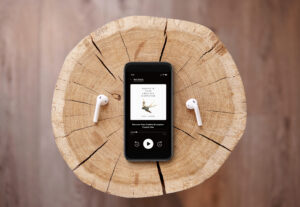 Audiobook of Discover Your Creative Ecosystem on an iPhone with earbuds sitting on a log