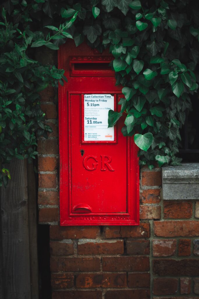 Red UK Postbox on a brick wall with ivy growing above
