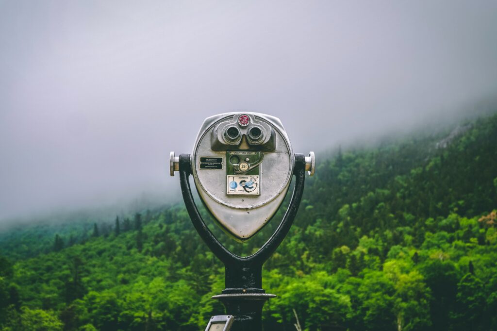 A tower viewer is a telescope or pair of binoculars permanently mounted on a stalk. Misty mountains beyond.