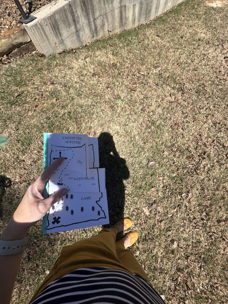 A hand holding my Choose Your Adventure zine while wearing colorful yellow pants, striped shirt, and yellow shoes.