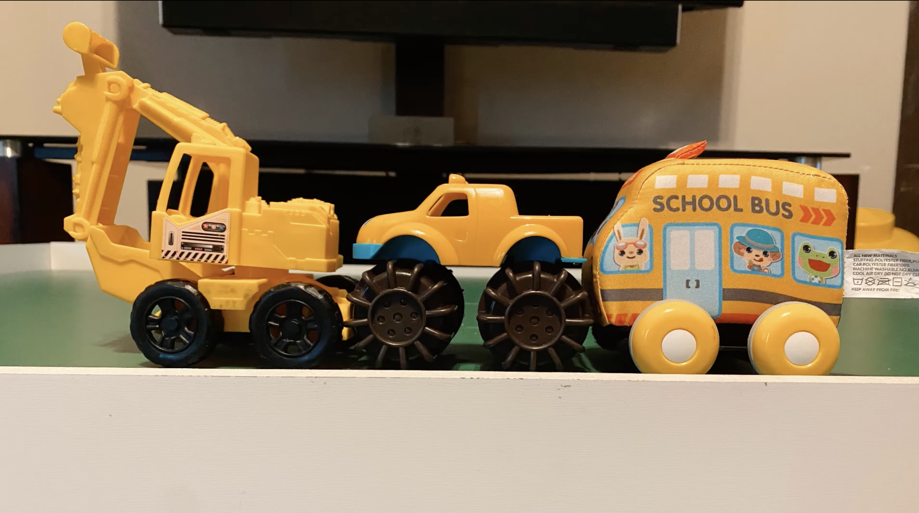 Three yellow toddler vehicles in a line: a digger, a monster truck, and a school bus.