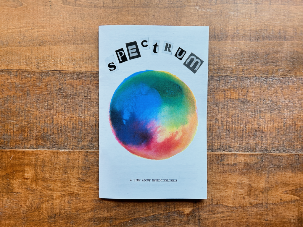 Spectrum: a zine about neurodivergence. Paper zine with magazine cutout letters and a watercolor spectrum with a rainbow of colors blending into one another.