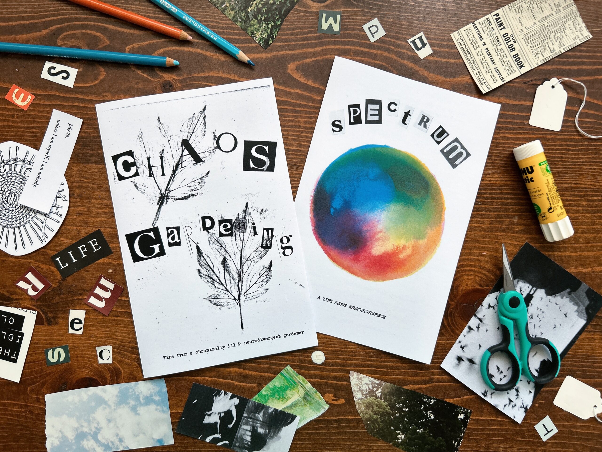 Two zines and magazine clippings on a wooden desk with scissors, gluestick and pencils. Both zines titles are cut out magazine letters: Chaos Gardening with leaf rubbings and Spectrum with a hand painted watercolor color wheel.