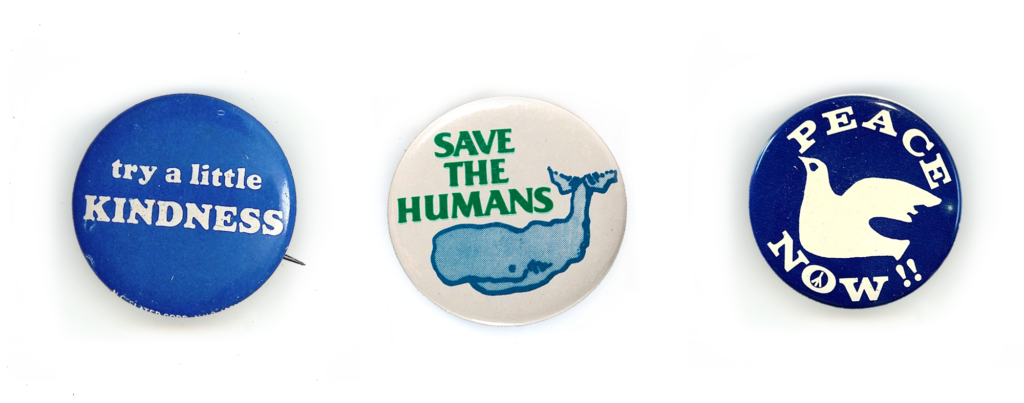 Three vintage protest pins: Try a little kindness (white text on blue.) Save the humans (green text on white and a blue whale.) Peace now (white dove on dark blue.)