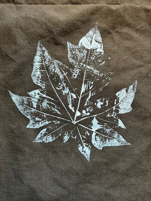 White test print of a smaller papaya leaf on a brown pillowcase