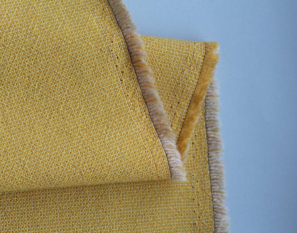 Closeup of the edge of a yellow cloth with holes from tenterhooks clearly visible