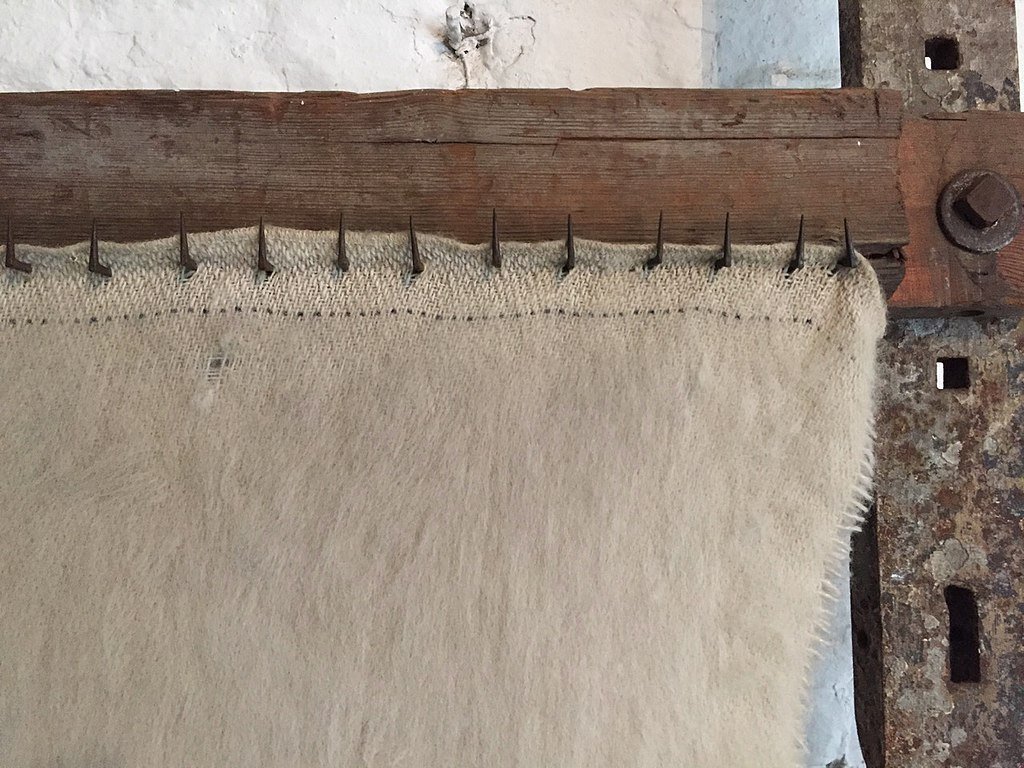 Closeup photography of a wooden frame with wickedly sharp hooks piercing light brown cloth