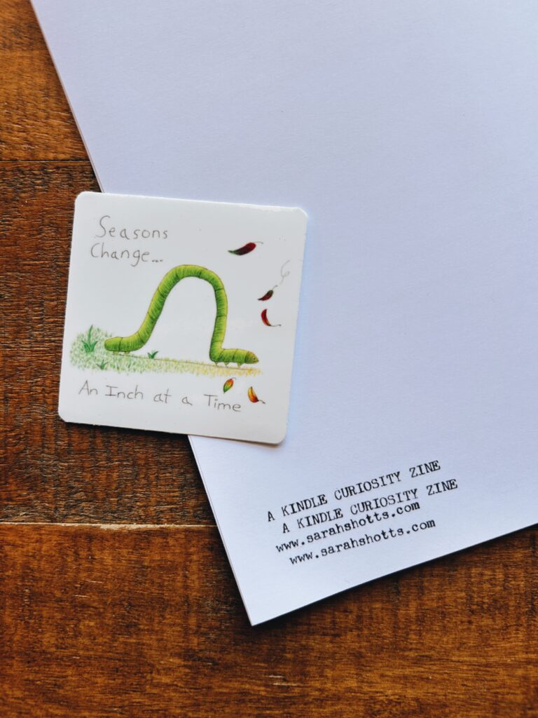 Sticker laying on back of zine depicts a drawing of an inch worm. It says seasons change an inch at a time.

The zine itself says Kindle Curiosity Zine. sarahshotts.com