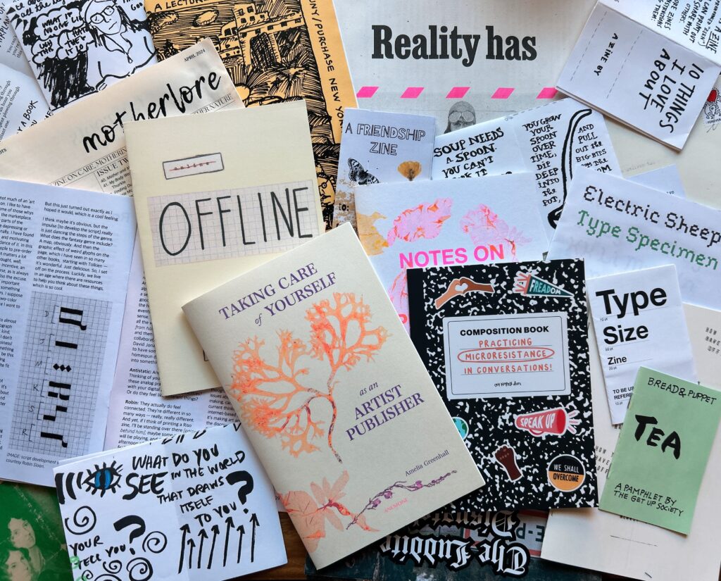 Zine collection spread on table. Visible titles include: Offline, Taking Care of Yourself as an Artist Publisher, Practicing Microresistance in Conversations, Tea, Reality Has, Motherlore, etc. Zines are various sizes and colors. Many have black sharpie on white paper appearance. Others are typed. The most visible are a bright neon risograph texture of seaweed (on the artist publisher book) and a composition book style (the microaggressions book.) Links to each zine are listed below.