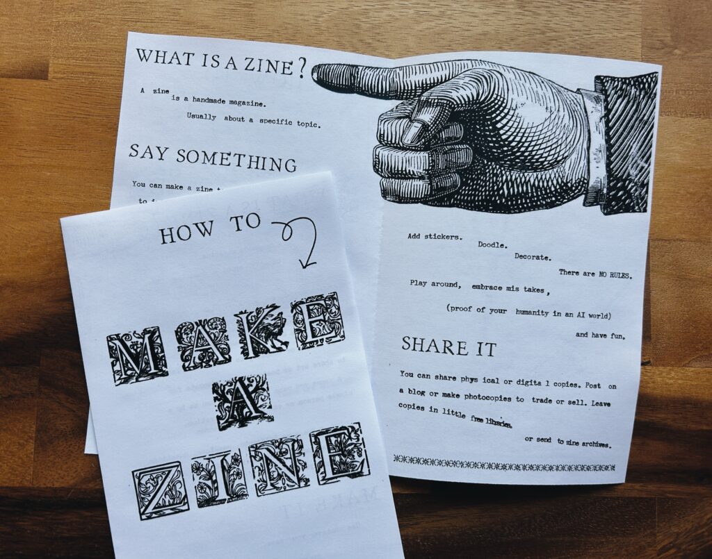 Black and white photograph of Make a Zine zine using vintage text and an illustrated pointing hand. Visible text reads: What is a zine? A zine is a handmade magazine. Usually about a specific topic. Say Something. Share it. You can share physical or digital copie. Post on a blog or make photocopies to trade or sell. Leave copies in little free libraries or send to zine archives.