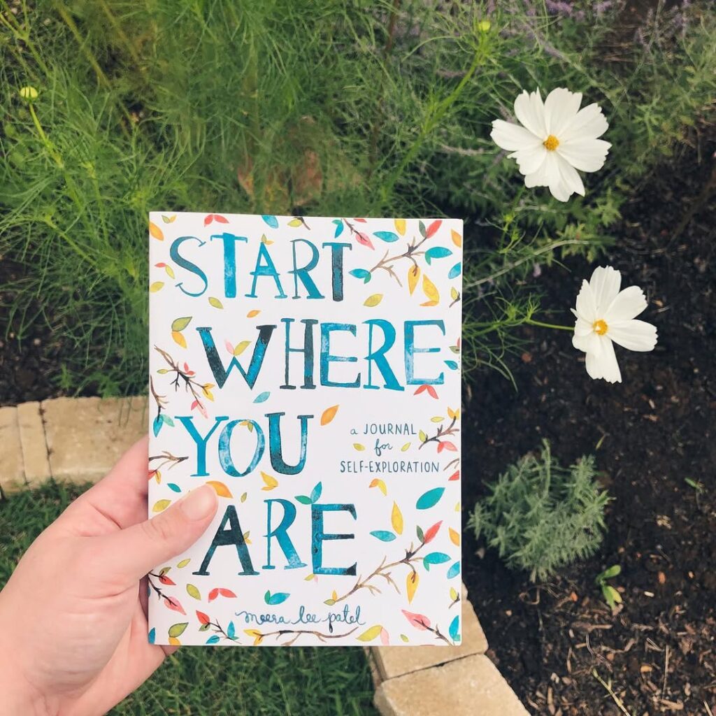 Start where you are book. Held over an imperfect garden with white cosmos nodding in the background.
