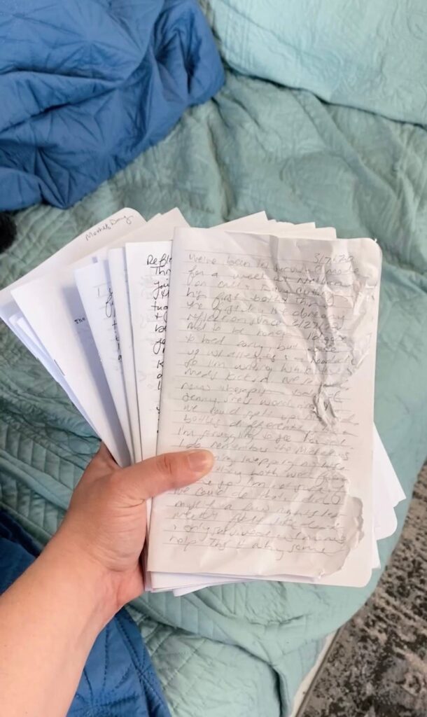 Holding a handful of journal inserts over a seafoam bedspread. The top one is wrinkled and slightly chewed.