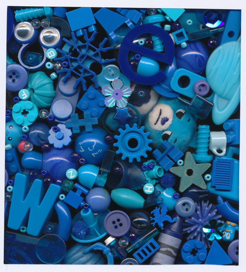 Tiny blue objects, buttons, beads, and toys in all different shades piled on top of each other. Grumpy Care Bear peeks through and a letter W is prominently visible.