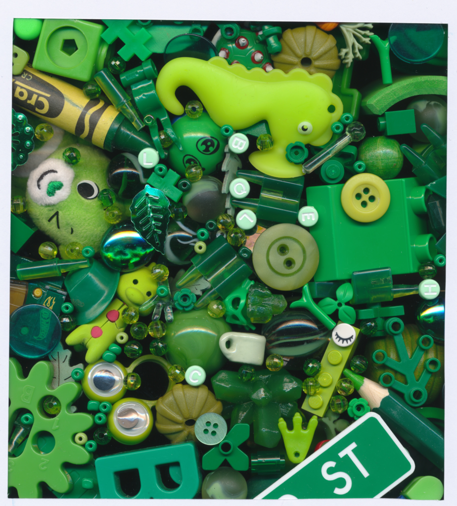 Tiny green objects, buttons, beads, and toys in all different shades piled on top of each other. Lime green seahorse, green crayon, and Lucky Care Bear are prominent.