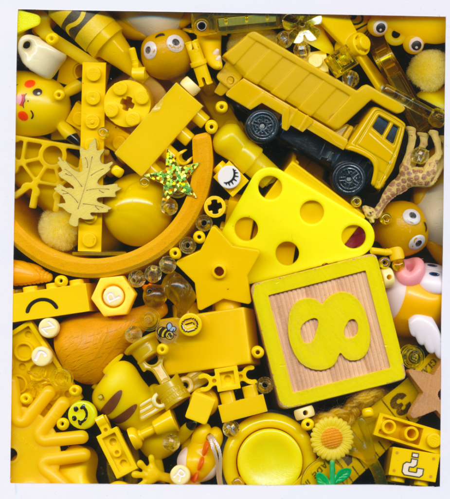 Tiny yellow objects, buttons, beads, and toys in all different shades piled on top of each other. Wooden number 8 block, yellow dump truck, and Pikachu are prominent.